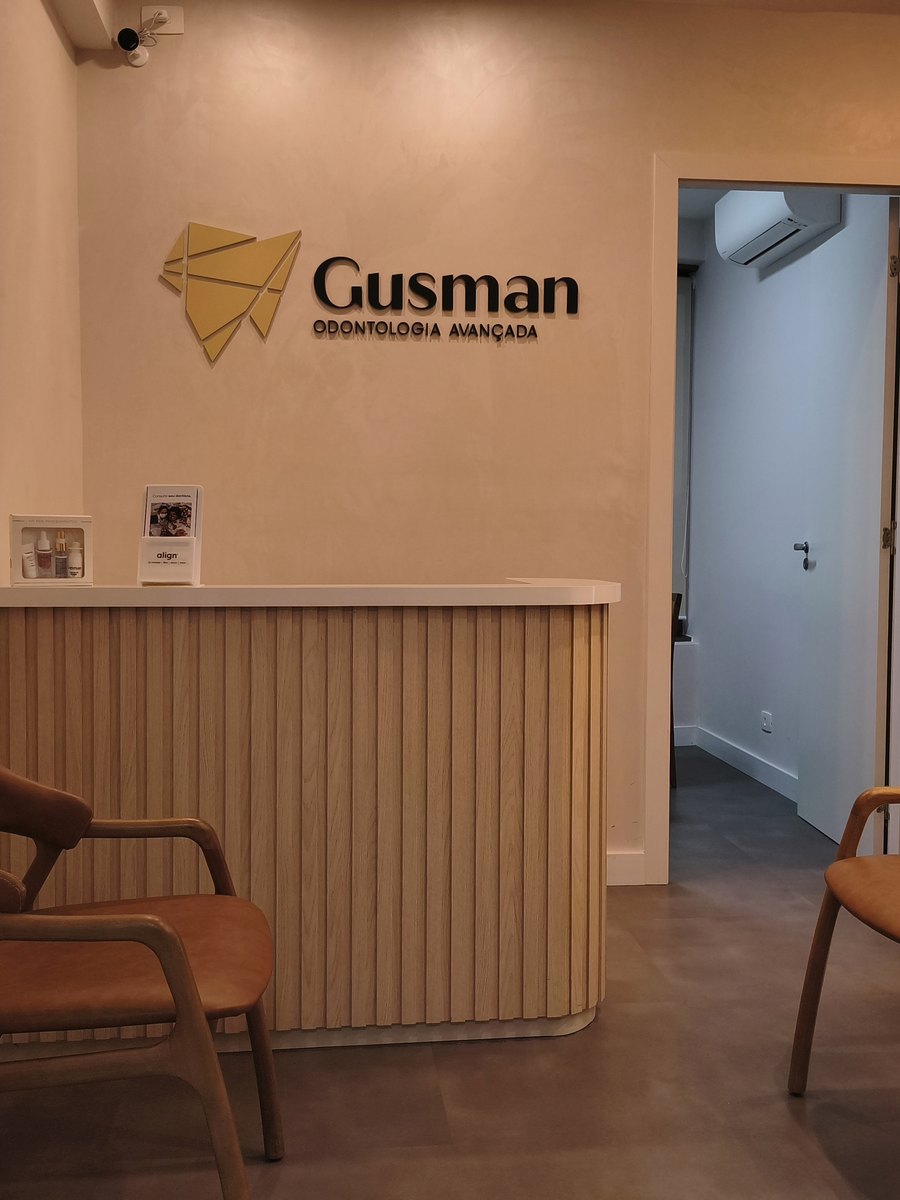 Recepção da Clínica Gusman, com balcão de madeira ripada, poltronas e o logotipo na parede